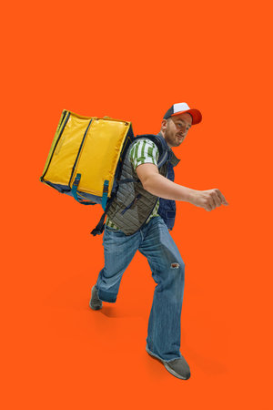 Excited delivery man with yellow backpack on back hurry up to customer against vibrant red...