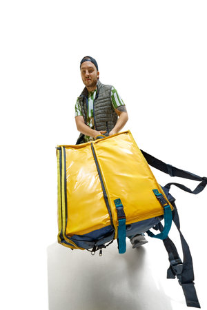 Wide angle photo of young man, courier, dressed casually and carrying huge food delivery pack...