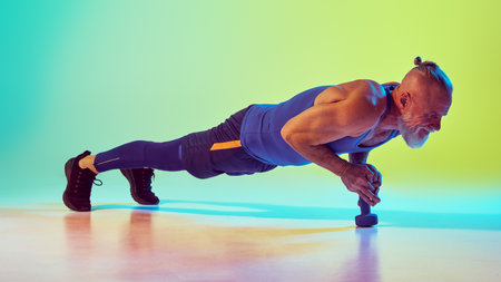 Muscular, strong, senior man in sportswear training with dumbbell, standing in plank against...