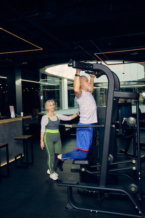 Senior sportive man in sportswear training in gym, doing pull-up exercises in modern gym with...