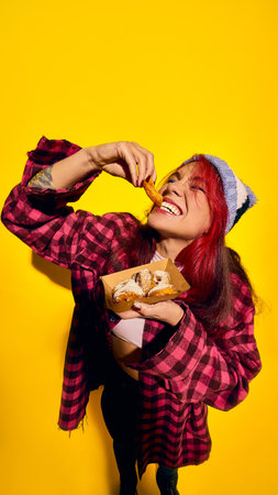 Happy, positive young women in checkered shirt and knitted hat, emotional eating sweet mini donuts with powdered sugarの写真素材