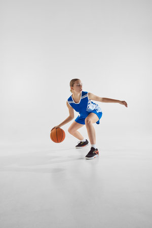 Dynamic image of teen girl in motion with ball, wearing blue uniform, competing for the victory, playing against white studio backgroundの写真素材