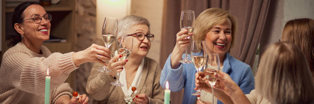 Group of lively friends, elderly women meeting at home, sitting in cozy warmly-lit living room, talking and drinking wineの写真素材