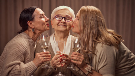 Happy Mothers day. Two elderly women, daughters greeting their old mother with her day, drinking wine, laughing, showing respect and loveの写真素材