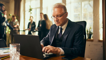 Focused senior businessman typing on laptop during professional networking event, showcasing dedication and efficiency.の写真素材