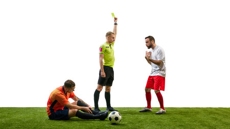 Referee showing yellow card to arguing man, while opponent player sitting on floor with outstretched...
