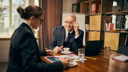 Personal consultation. Focused business conversation between senior leader and young professional discussing strategy in a modern office.の写真素材