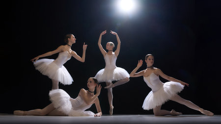 Four young girls, ballet dancers performing dramatic and elegant dance under spotlight, showcasing beauty of classical dance and artistryの写真素材