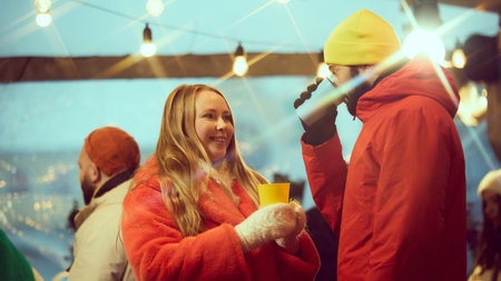 Cheerful young woman in vibrant orange standing next to man in yellow hat and red jacket, talking,...