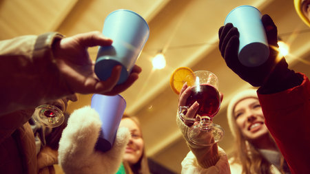 Bottom view of group of people laughing, friends gathering outdoor for holiday celebration, drinking hot drinks, clinking glasses in celebratory toastの写真素材