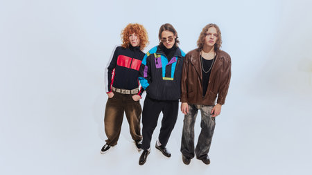 Three stylish young men in their early 20s, wearing colorful windbreakers, leather jacket and casual...