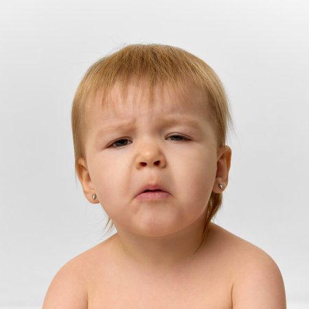 Close-up portrait of baby girl, toddler with an expressive, slightly puzzled face sits against...
