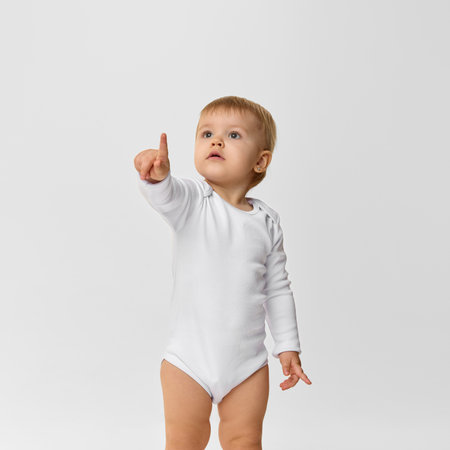 Baby girl, toddler in white bodysuit looking and pointing upwards with interest and curiosity...