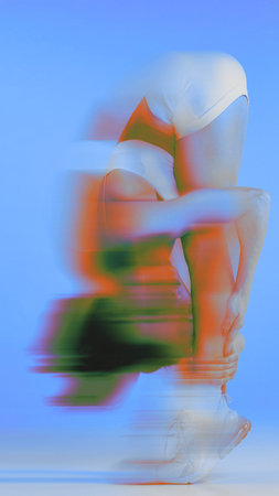 Conceptual art design. Grace in movement. Young sporty woman showing her flexibility during training in neon glow with motion blur effect.の写真素材