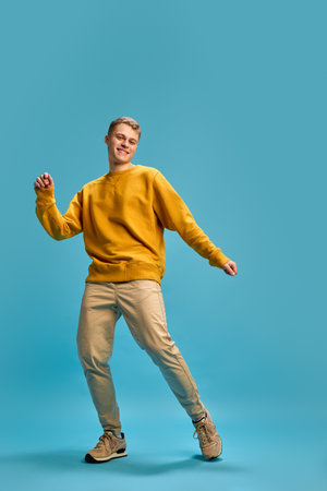Man mid-dance, shifting confidently with playful energy, smiling as he transitions through movements, fully immersed in dynamic motion against blue background.の写真素材