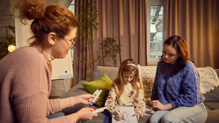 Psychologist and mother using art technique in communication with child, little girl drawing and therapist analyzing. Maintaining communication with kidsの写真素材