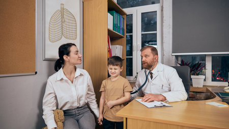 Bearded man, doctor listening to child lungs with stethoscope in medical office. Mother and child visiting pediatrician for health checkupの写真素材
