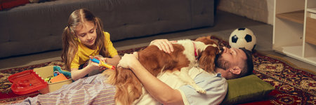 Girl in yellow shirt playing doctor with her father and dog, who lying on the carpet, taking injections with toy medical kitの写真素材