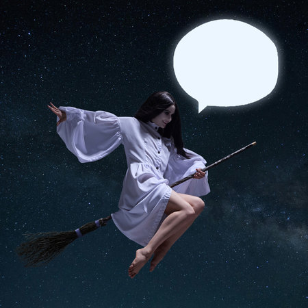 Witch with black hair, in flowing white dress sits on broom and flies in starry sky with a speech bubble ready for custom text.の写真素材