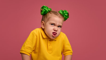 Portrait of emotive preschool girl, child in yellow shirt and braided buns, making funny faces, grimacing, playing against pink studio background.の写真素材