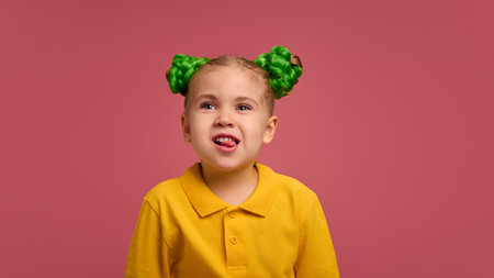 Portrait of adorable child, preschool girl wearing yellow polo shirt, with braided buns hairstyle emotionally grimacing against pink studio background.の写真素材