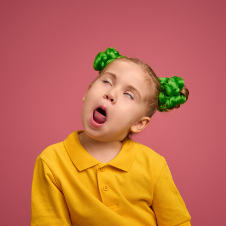 Portrait of emotive preschool girl, child in yellow shirt and braided buns, making funny faces, playing against pink studio background.の写真素材