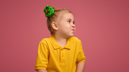 Portrait of playful child, preschool girl in yellow shirt and braided buns hairstyle emotionally making funny faces against pink studio background.の写真素材