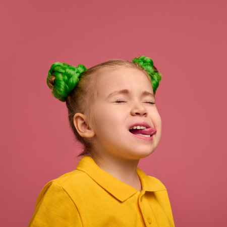 Portrait of adorable child, preschool girl wearing yellow polo shirt, emotionally grimacing against pink studio background.の写真素材