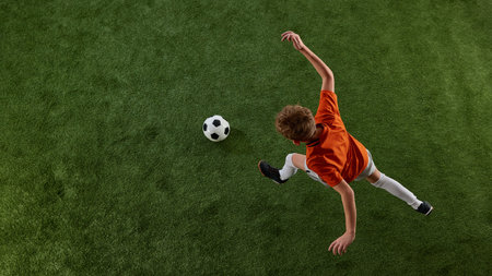 Image viewed from above of boy, soccer player in orange jersey and white shorts in motion of green field, playing, dribbling ball. Training activityの写真素材