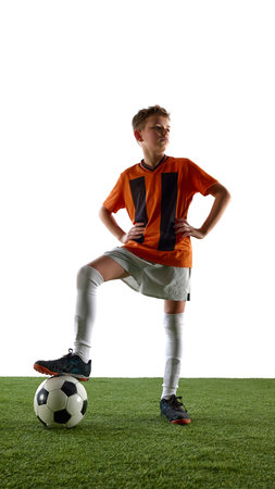 Full-length portrait of boy, soccer player in orange jersey and white short, with leg on ball, standing with confidence after successful gameの写真素材
