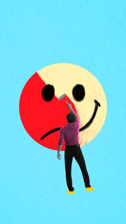 Man painting sad face into smiley on large emoji against blue background, symbolizing digital masking of real emotionsの写真素材