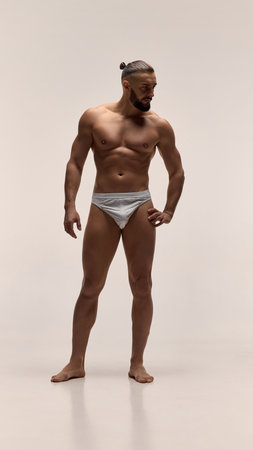 Front view full-length portrait of muscular man posing confidently shirtless in white underwear showing defined physiqueの写真素材