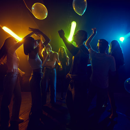 Lively group of young friends dancing, enjoying neon-lit party, filled with laughter and vibrant...