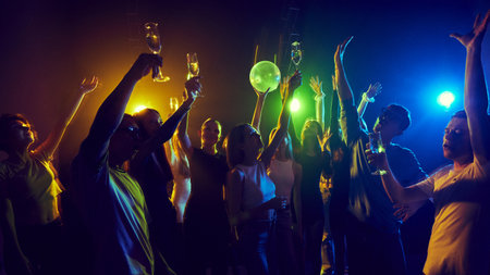 Group of cheerful young people celebrating together in vibrant neon-lit club with colorful neon lights.の写真素材