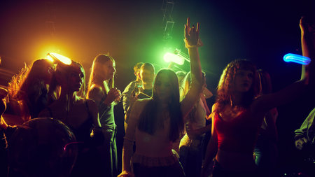 Young people, men and women gathering together, attending concert, party, cheerfully dancing and...
