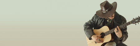 Rugged cowboy in leather coat and hat, playing acoustic guitar with focused expression, looking down...