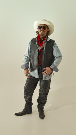 Stylish cowboy in white hat, sunglasses, and red bandana, standing confidently in leather vest and...