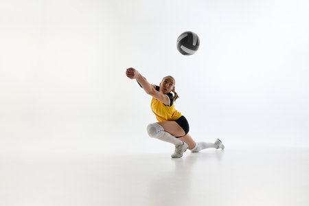 Dynamic image of young woman, volleyball player training, growing skills and focus, hitting ball in motion against white studio background.の写真素材