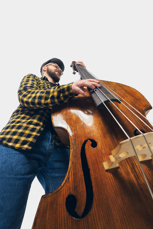 Low angle view of stylish double bass player in checkered shirt leaning into deep groove, fingers...