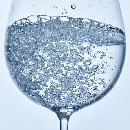Close-up photo of water filled with bubbles in clear stemmed glass against soft background. Mock up.