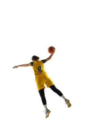 Back view of female basketball player in yellow jersey and black shorts performing slam dunk...