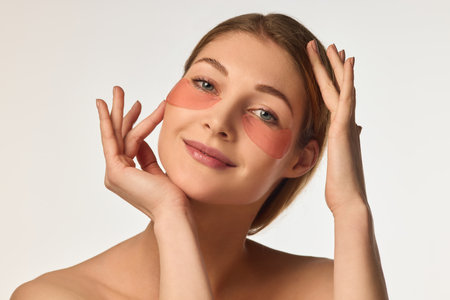 Portrait of attractive, happy, young woman with glowing, healthy skin, posing with under eye patches against white backgroundの写真素材