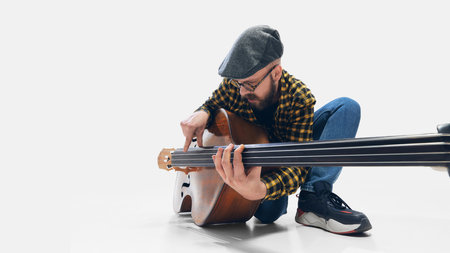Focused man, musician crouching, playing double bass, deeply immersed in rhythm on minimalist white backdrop.の写真素材