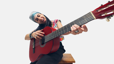 Low-angle close-up of female guitarist in colorful outfit, playfully leaning forward while strumming red guitar.の写真素材