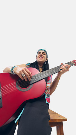 Low angle view of stylish woman, dynamically paying red guitar against white background.