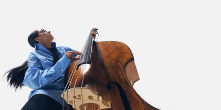 Low-angle image of young woman, double bass player in oversized blue shirt, elegantly playing with focused expressionの写真素材