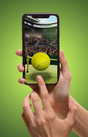 Person using smartphone to access tennis sports app, translation of live match updates. Tennis ball and court with filled stands.の写真素材