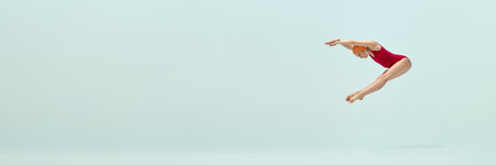 Woman in red vintage swimsuit and orange cap captured mid-air dive with perfect form against light blue backgroundの写真素材