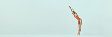 Woman in orange swimsuit and teal cap striking diving pose on light blue background.の写真素材