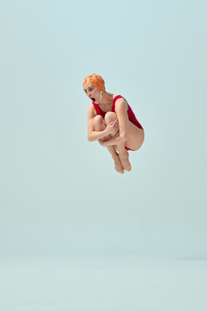 Diver in red vintage swimsuit and orange cap making cannonball pose in air with comic expressionの写真素材